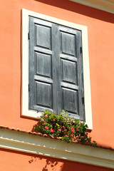 Picturesque vintage window with carved wooden blinds and flowers in bright orange wall