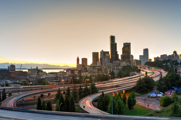 Seattle modern skylines and rush hour traffic on highway I-90 and I-5 interchange. Nearby density of homeless tents and tiny shelter in trees and foreground on the left. Problem of urban life concept