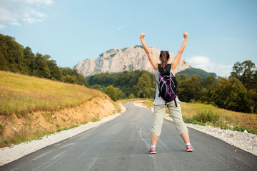 Fototapeta premium Young woman standing with arms raised in the air and enjoying the view of the surrounding peaks. Tranquility in nature.
