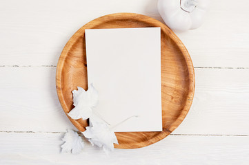 Wooden place with white sheet of paper. White pumpkin, berries and leaves on a mockup autumn wooden...