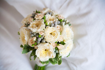 Tender rustic wedding bride bouquet with roses and buttons  lies on a white bed. close up