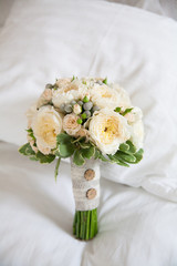 Tender rustic wedding bride bouquet with roses and buttons  lies on a white bed
