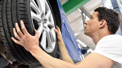 Reifenwechsel in einer autowerkstatt // tyre change in a car repair shop - worker assembles rims on...