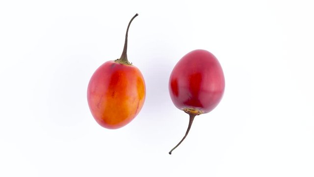 Top view from above of a two whole ripe tamarillo fruits. Rotating on the turntable isolated on the white background. Close-up. Macro.