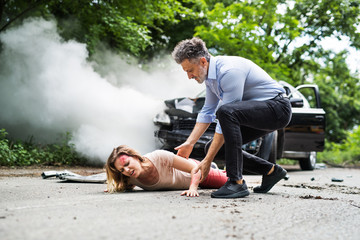 A man helping a young woman lying on the road after a car accident.