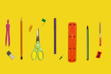 row of different school and office stationary and gadgets lying on a yellow background
