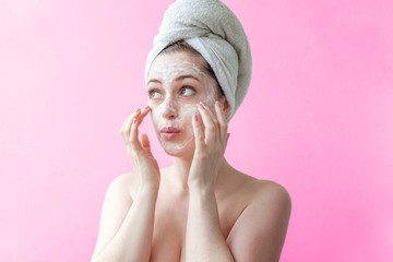 Beauty portrait of a smiling brunette woman in a towel on the head applying white nourishing mask...