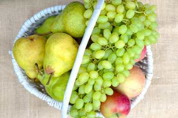 Organic fresh fruit in a white wicker basket. Apples, pears, grapes, peaches, plums.