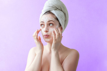Beauty portrait of a smiling brunette woman in a towel on the head applying white nourishing mask...