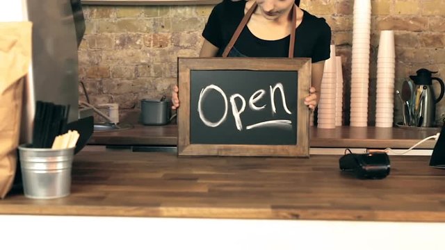 Female coffee shop owner looking at chalkboard with sign open on it, smiling and looking at camera. Steadycam shot.