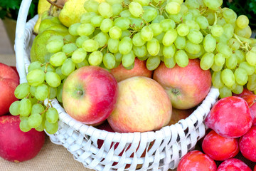 Organic fresh fruit in a white wicker basket. Apples, pears, grapes, peaches, plums.