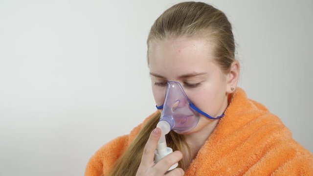 Teenage girl using nebulizer with breathing mask at home inhaling the medication