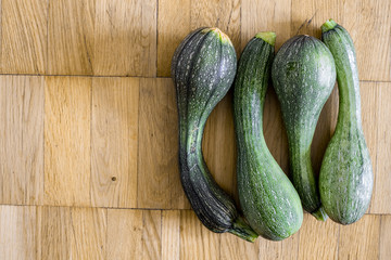Four green zucchini on a light brown wooden plane