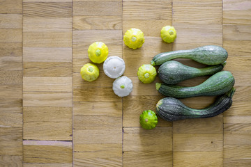 Four green zucchini with small scallop squashes over the light brown wooden background