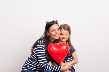 Fototapeta na wymiar A small girl and her mother holding a red heart in a studio.