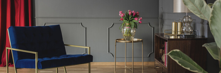 A luxurious, modern, navy blue armchair and a bouquet of pink tulips on a golden table in an...