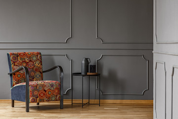 Patterned armchair next to table against grey wall with molding in living room interior. Real photo