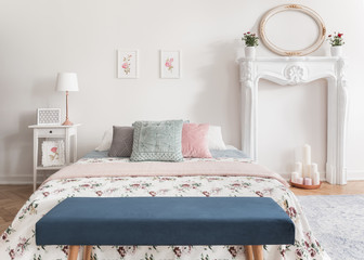 Blue bench in front of patterned bed with pastel cushions in white bedroom interior with mirror....