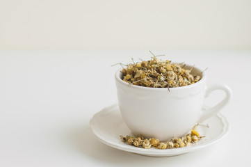 Herbal chamomile drink. Dried chamomile tea in a white small cup on white table