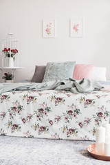 Patterned sheets and pillows on bed in feminine bedroom interior with posters and roses. Real photo