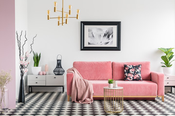 Pink blanket on settee in white living room interior with plants and checkered floor. Real photo