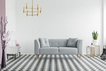 Flowers and gold chandelier in spacious living room interior with grey sofa on checkered floor....