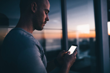young men standing in front of windows with smartphone while sunset