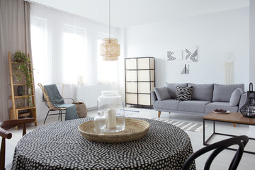 Candle on table in white flat interior with plant on cabinet and pillow on grey sofa. Real photo