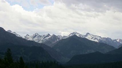 Layers of snow-covered mountain peaks leading off into the distance with stormy clouds overhead