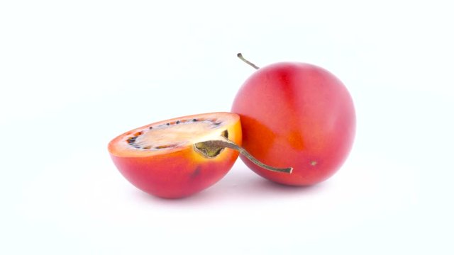 One and a half of mature tamarillo fruits quickly rotating on the turntable isolated on the white background. Close-up. Macro.