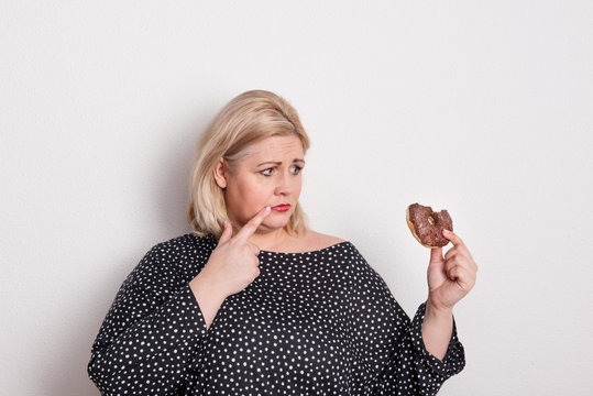 An Attractive Overweight Woman Eating A Donut, Feeling Guilty.