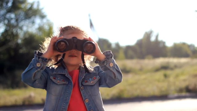 Child girl looking through binoculars and watching the nature
