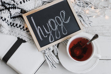 Naklejka premium Cup of red hibiscus tea, white book, lights, warm knitted blanket and blackboard with text 