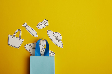 top view of blue shopping bag with paper clothes on yellow background