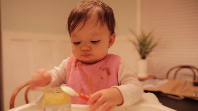 Baby Feeding Herself Baby Food in High Chair