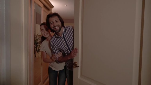 Guy opens the white door. Girl stands behind him. They are happy. People welcome to their new home. Camera enters apartment.