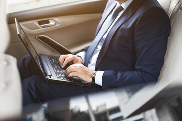 a young business man in a suit is sitting in the back seat of a business car with a laptop and a...