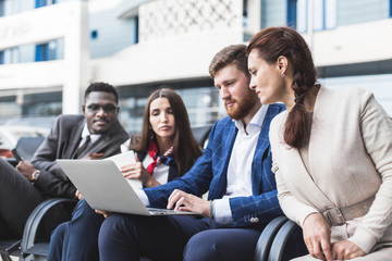 Group of happy diverse male and female business people team in formal gathered around laptop computer in bright office against the background of a glass building