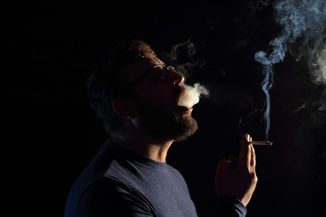 Obraz premium man brunette with a cigarette in the dark, a lot of smoke