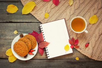 notepad open, mug with tea and autumn leaves on a wooden background. flat lay