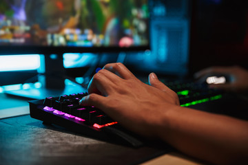 Hands of young gamer man playing video games on computer in dark room, using backlit colorful keyboard © Drobot Dean