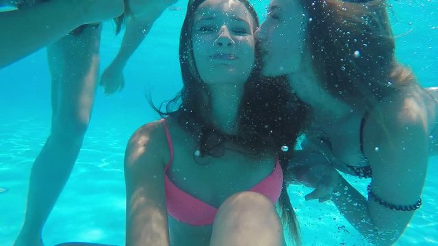 Two girls kiss their girlfriend on the cheek under the water in the pool