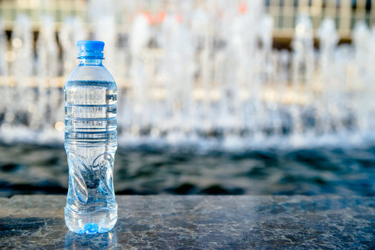 A Bottle Of Drinking Water Stands On The Background Of The Fountain 