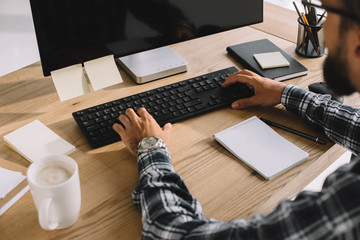 cropped shot of bearded man in plaid shirt using computer at workplace