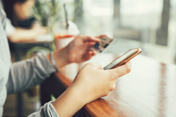 Online payment concept, Woman hands holding using cellphone and credit card for online shopping at coffee shop in the afternoon