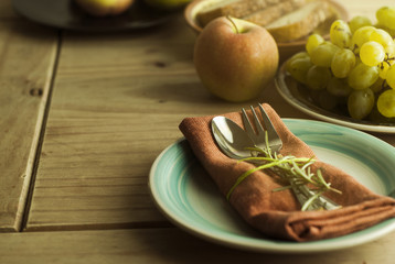 Fork and spoon over napkin, with a twig of rosemary. Fruits and bread on background. Healthy food. Rustic wooden background. Food education.