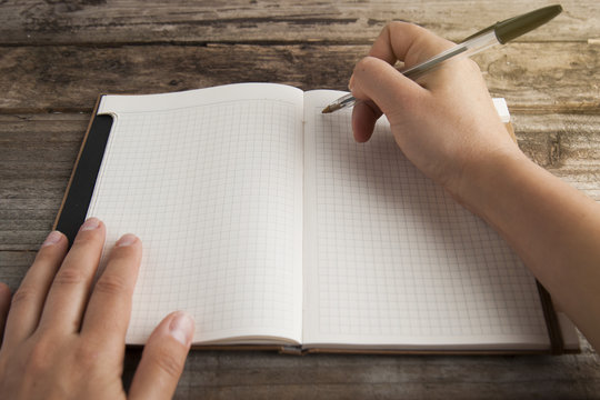 Work And Time Management, Planning Diary And Human Hand Holding A Pen Close-up Over Opened Note Book. Rustic, Old Textured Wooden Table. Copy Space. Back To School.