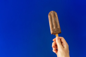 Chocolate ice cream on a stick on deep blue background.
