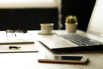 Creative workspace of a blogger. White laptop computer & folded eye glasses on wooden table in loft style office with black brick walls. Designer's table concept. Close up, copy space, background.