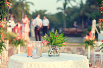 Close up dinner table tropical style set on the beach in sunset time Thailand. Beautiful delicate wedding decoration with tropical flowers and fruits. Wedding setting table on the beach.